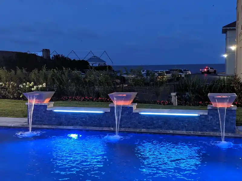 Three copper scuppers pouring into a lit pool at dusk