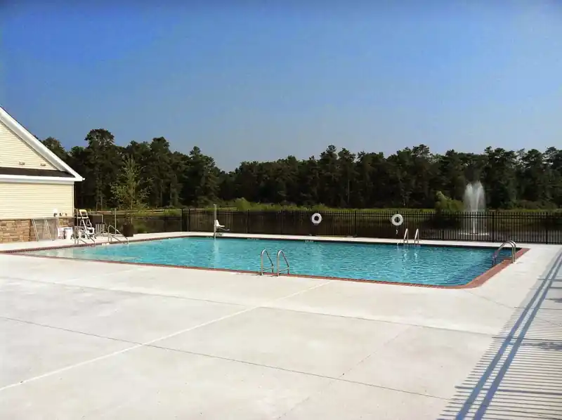 Clear rectangular pool on a swept concrete deck beside a lake