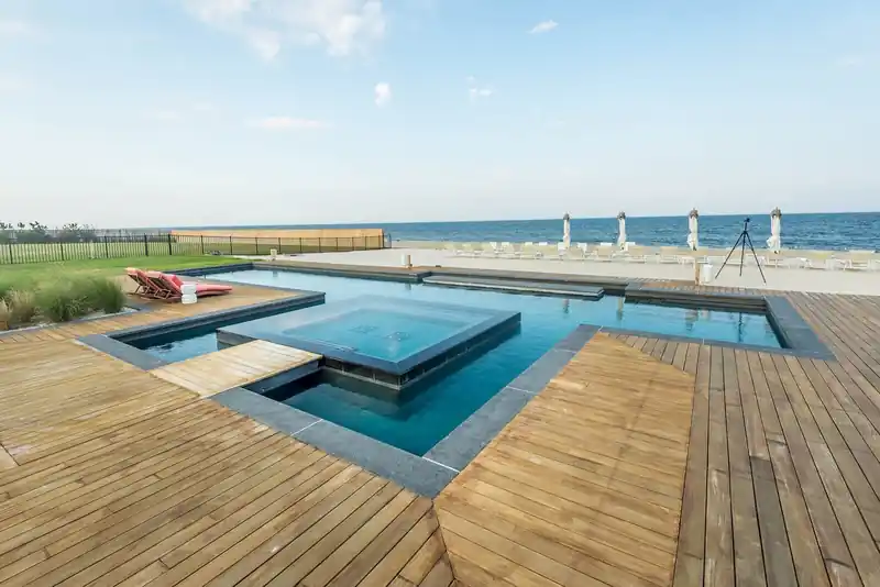 Geometric pool with a raised square spa on a timber deck, the beach and ocean beyond