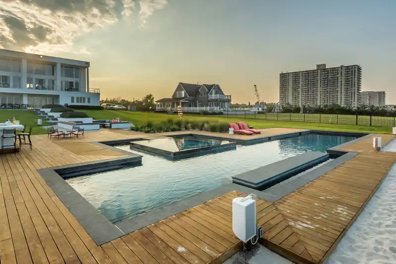 Oceanfront geometric pool on a timber deck at golden hour, a high-rise beyond the beach