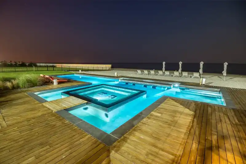 Oceanfront geometric pool glowing at night against a dark sky