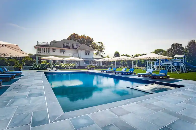 Rectangular pool set in a bluestone patio beside a waterfront house
