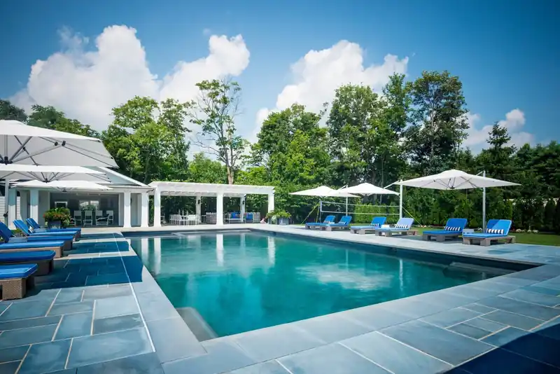 Backyard pool with a pavilion, white loungers and blue umbrellas
