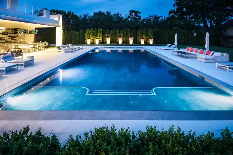 Pool lit at dusk with a built-in lounge and outdoor TV wall