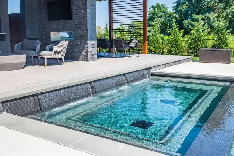 Spa fed by sheer waterfalls from a dark stone wall, outdoor kitchen behind