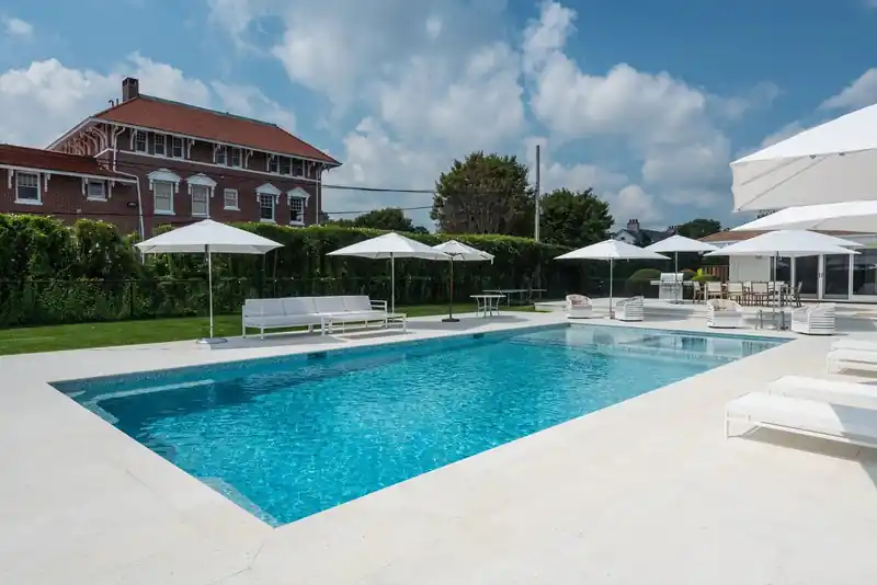 Long rectangular pool with umbrellas and loungers before a brick house